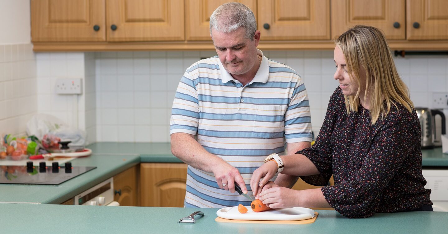 A blind man being guided how to cut carrots.