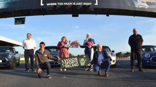 Staff pictured in front of cars holding Vision Sports banner