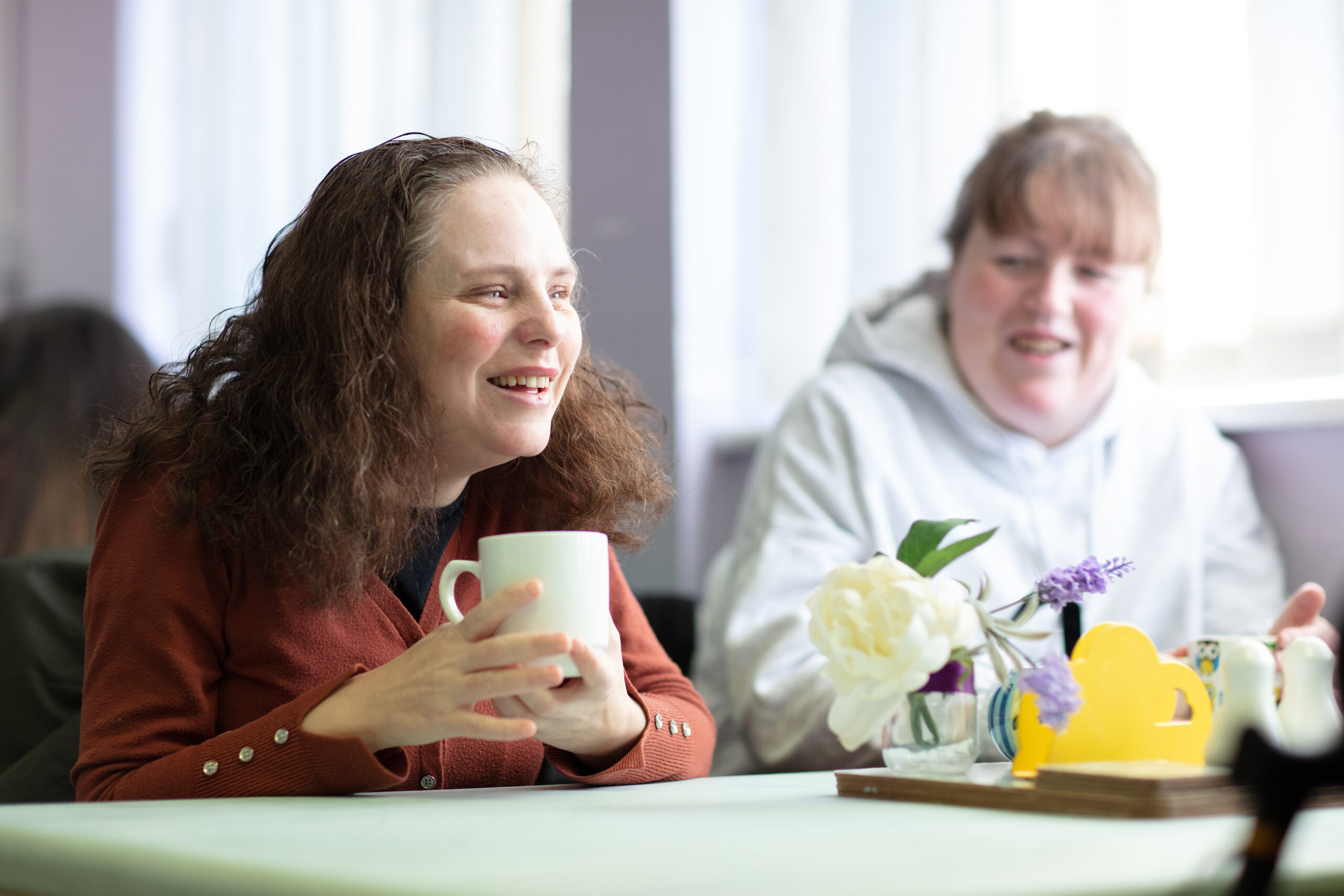 Two female Vision Ireland service users laughing as they engage in conversation while sitting at a coffee table