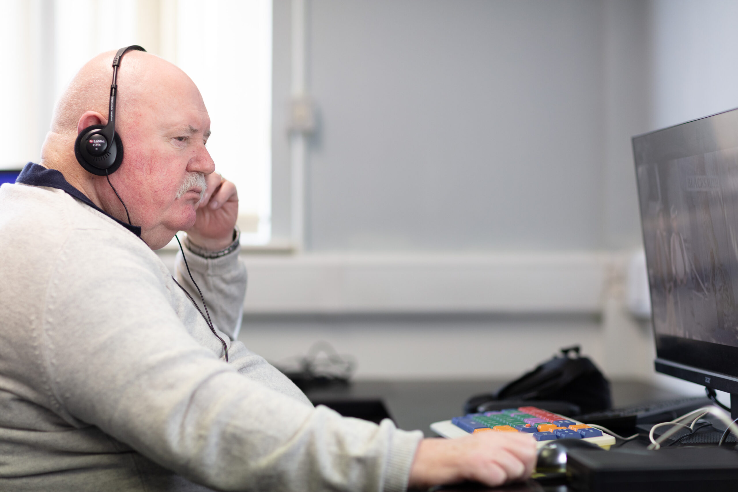 An Vision Ireland service user sitting at a computer using accessibility features as he wears headphones