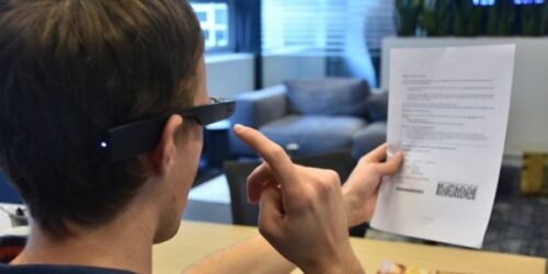 Man wearing Envision glasses to read text on sheet of paper