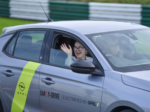 A Zero Limits participant waves through an open window to onlookers at the event while smiling as she is driving her dual control car
