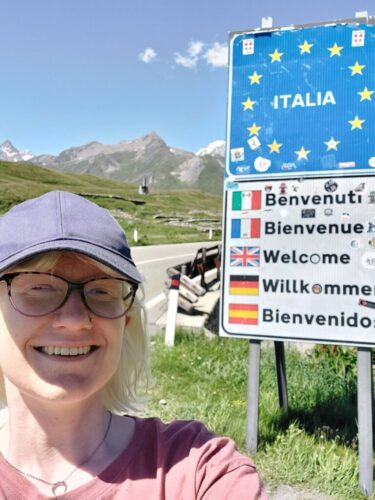 Aoife Doherty is wearing a cap and is visible in the bottom left hand corner of the picture. She is smiling in the selfie, the background of which includes a sign with the word welcome in different languages over another sign which reads Italia.