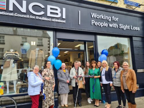 Ribbon cutting picture caption: Monaghan-based Vision Ireland service user Carmel Hill cuts the ribbon to open Vision Ireland's new, modern store and location in Carrickmacross. Carmel is cutting the ribbon outside the front of the store which is decorate with light and dark blue balloons. Carmel is surrounded by volunteers and members of Vision Ireland's retail team at the launch.