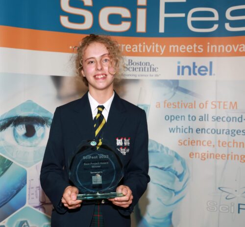 Maura Moore McCune stands in her school uniform and is holding a crystal award that she got at a science festival.