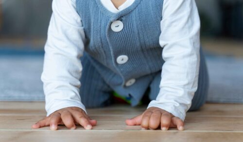 A close up of a baby crawling on a wooden floor. the baby is wearing a white and blue outfit.