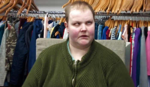 Brandan Laffan is standing in an Vision Ireland store and rails of clothing are visible behind him. He is wearing a green zip up cardigan.