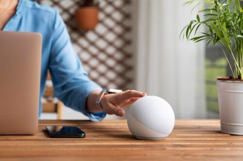 Person about to touch a smart speaker on their desk