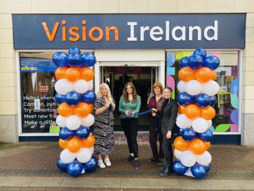 Four women from the Vision Ireland store in Limerick are standing between two pillars of blue, white and orange balloons which match the exterior colours of the store. They are cutting the ribbon to open the Limerick store outside the door of the shop.
