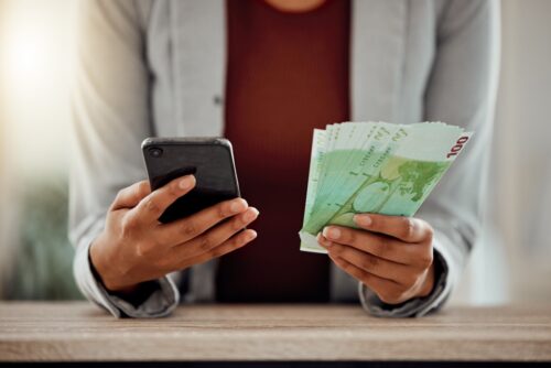 Person holding a phone and a wade of bank notes in separate hands
