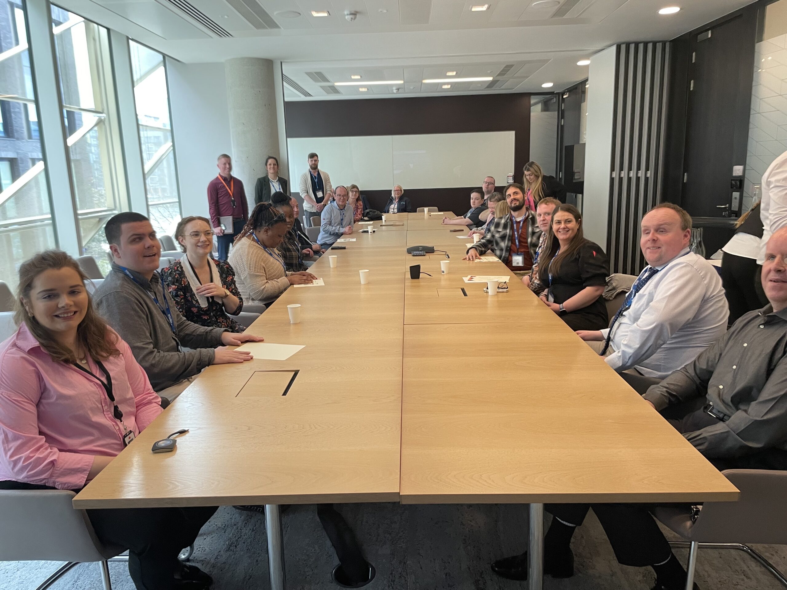 : Vision Ireland staff and National Training Centre students sitting around a long table in the meeting room in the Central Bank office. There are also a few staff members from Central Bank Present. Most people are looking at the camera and smiling.