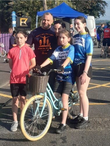 Image of three girls and a man wearing NCBI t-shirt participating in pedal for grace with cycle on tow.