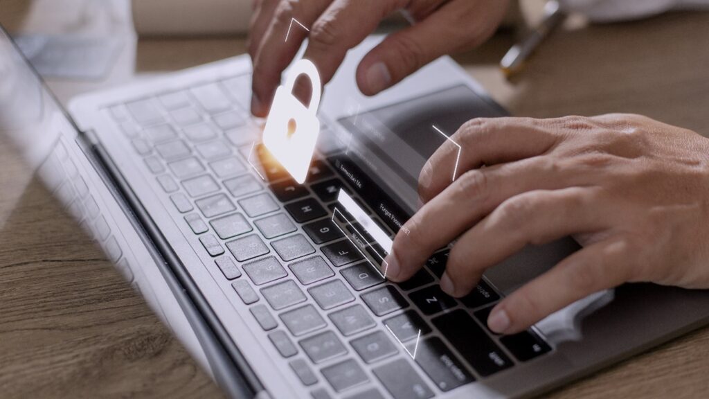 Pair of hands over a laptop keyboard with a padlock symbol featured above it.
